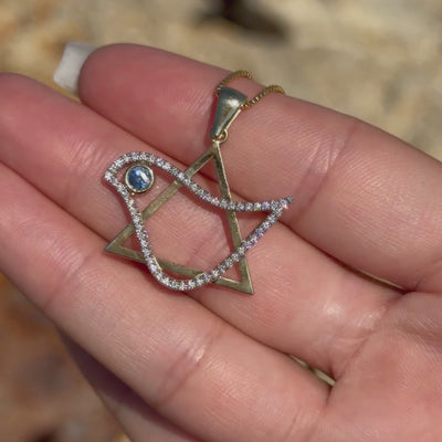 Two-tone Dove of Peace Legacy Pendant with a diamond-set dove and blue gemstone eye, held outdoors