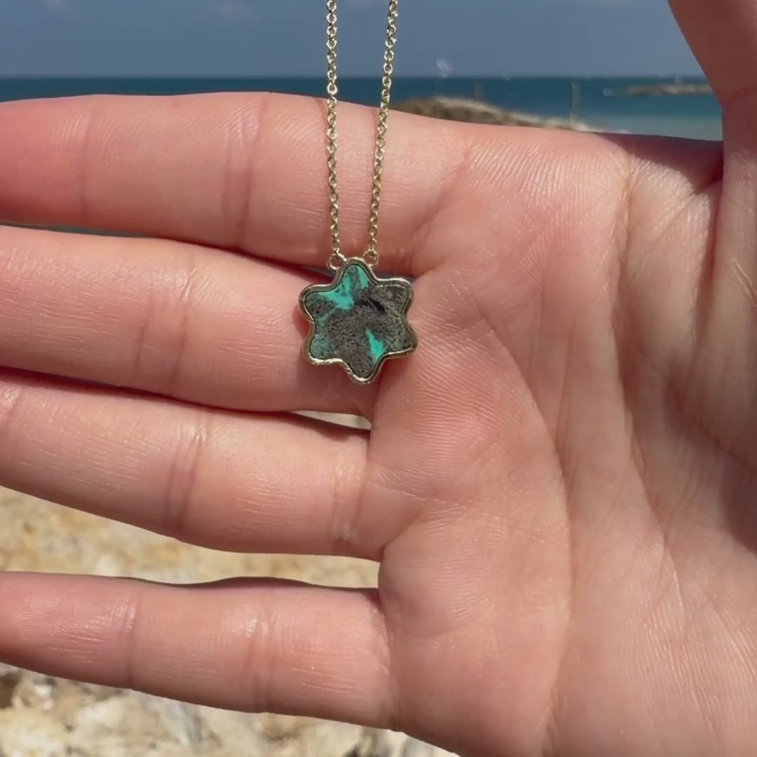 Tyferet Symbol Eilat Stone Necklace held outdoors with the Mediterranean Sea in the background